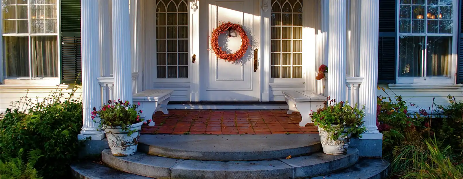 A colonial entry with lit sconces either side of the door