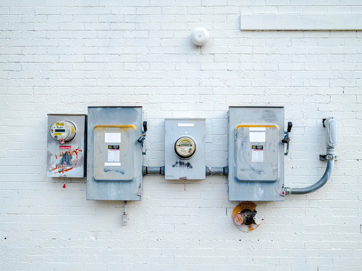 An electric meter between two service disconnects on a painted brick wall