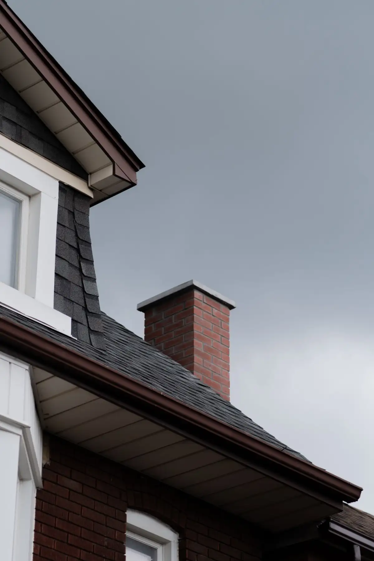 A shingled roof and brick chimney under a gray sky